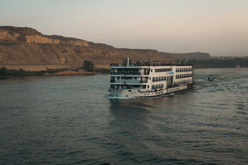 Author standing beside a river cruise ship with notebook in hand, smiling