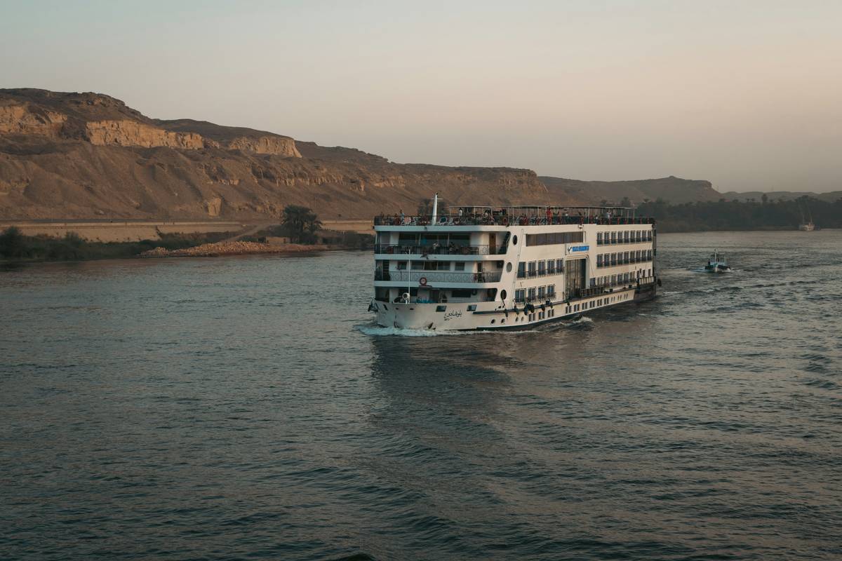 A modern river cruise ship docked at a cobblestone quay, with flood markers visible on nearby stone walls — river adventure policy